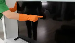 Osoba v oranžových rukavicích čistí obrazovku televize hadříkem.