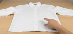 Ruka ukazuje na složenou bílou košili položenou na stole, příprava k žehlení nebo skládání.