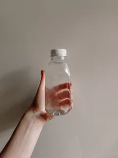 Ruka držící lahvičku s kapátkem na bílém pozadí